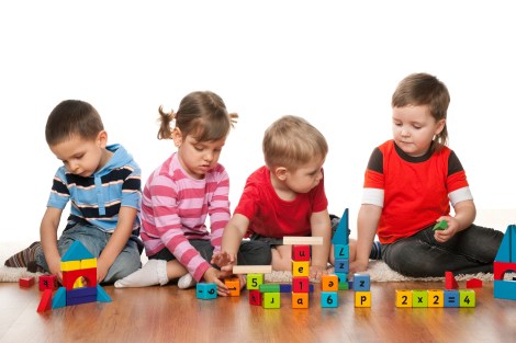 Four children are playing on the floor with blocks